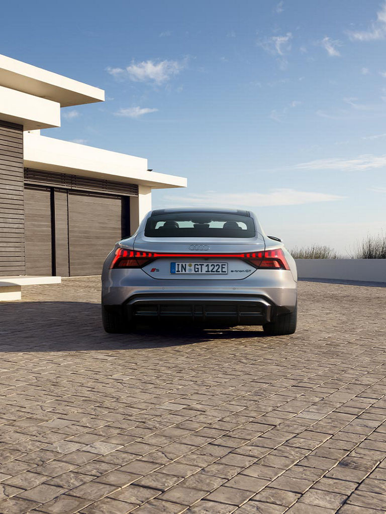 The rear view of the Audi S e-tron GT on a paved driveway. The continuous LED light strip and the sporty diffuser emphasize the dynamic design.